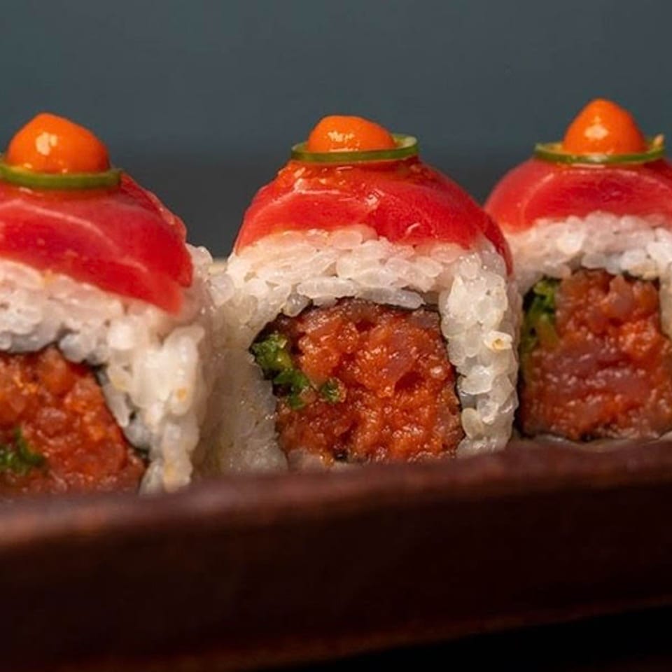 Three sushi rolls with red tuna, white rice, and orange topping on a dark plate.