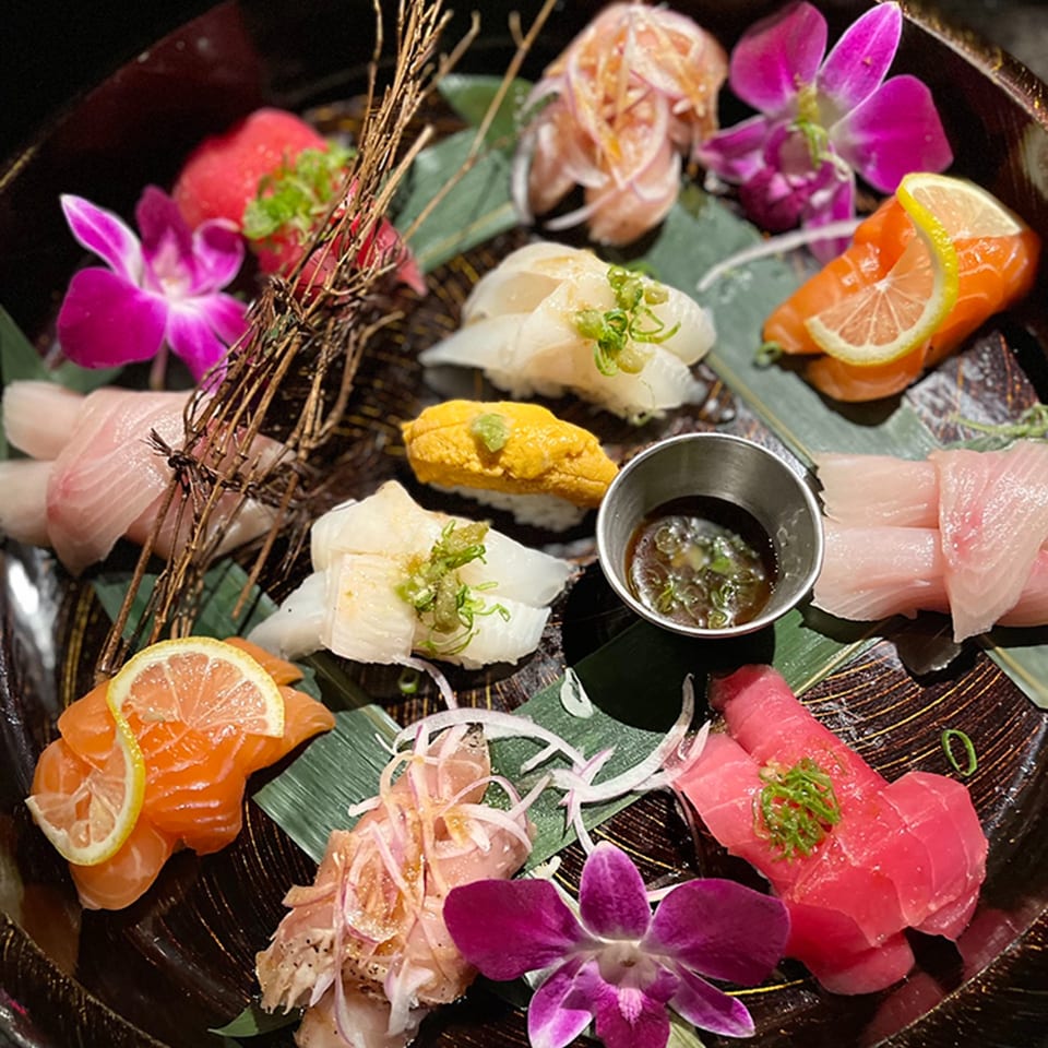 A platter of various sushi and sashimi, garnished with orchids, lemon slices, and green onions.