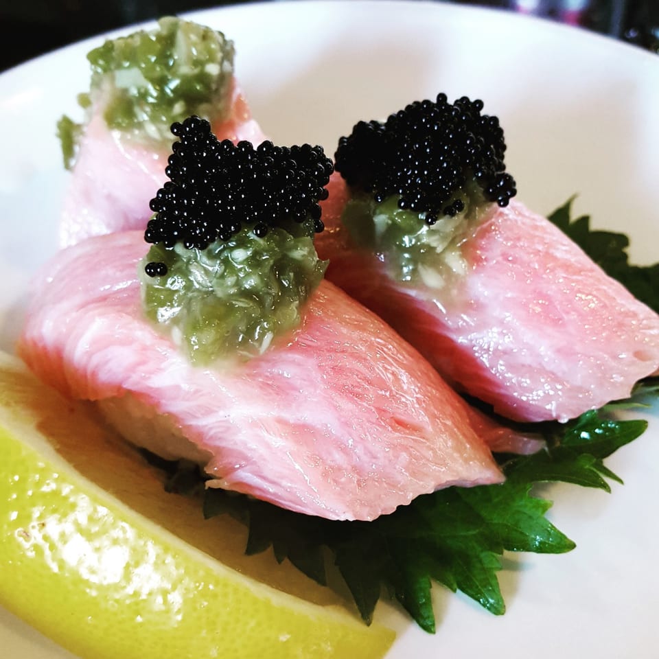 Three pieces of Tomoya Sushi & Izakaya's tuna nigiri with green sauce, black caviar, and a lemon wedge.